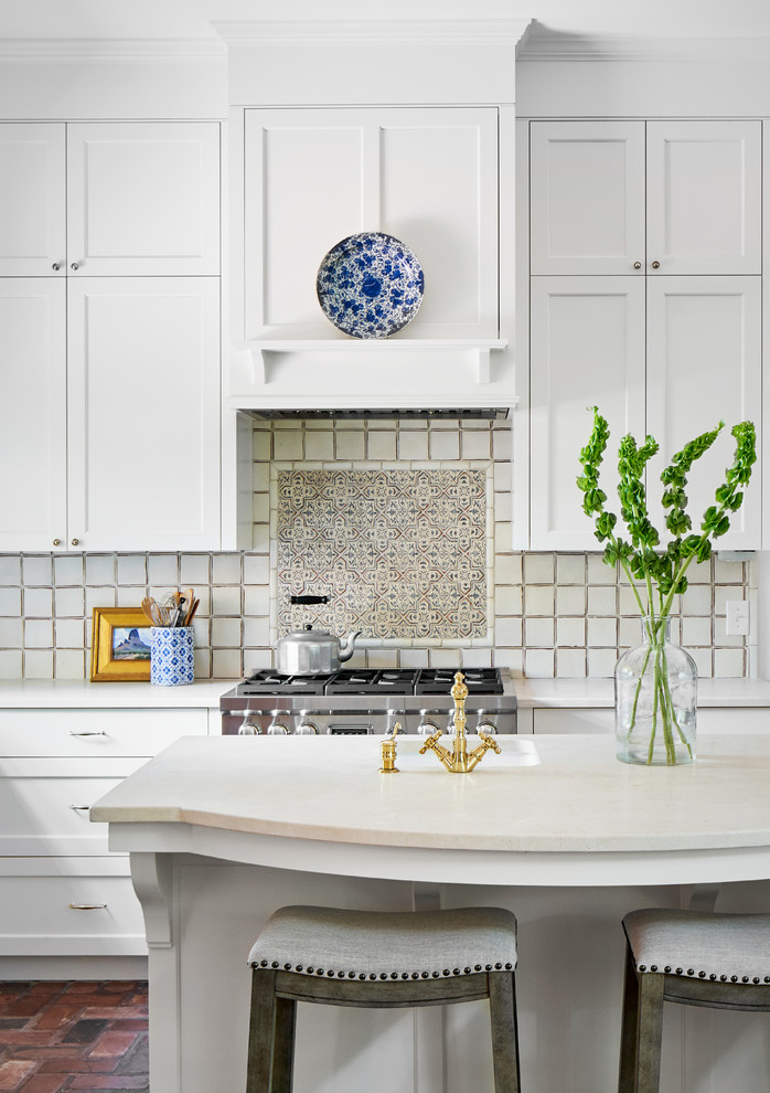 Photo of a mid-sized beach style l-shaped kitchen in Austin with an undermount sink, shaker cabinets, white cabinets, marble benchtops, white splashback, ceramic splashback, stainless steel appliances, brick floors, with island and white benchtop.
