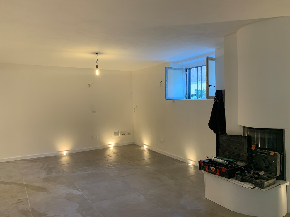This is an example of a mid-sized contemporary basement in Milan with white walls, grey floor, porcelain floors, a corner fireplace and a concrete fireplace surround.
