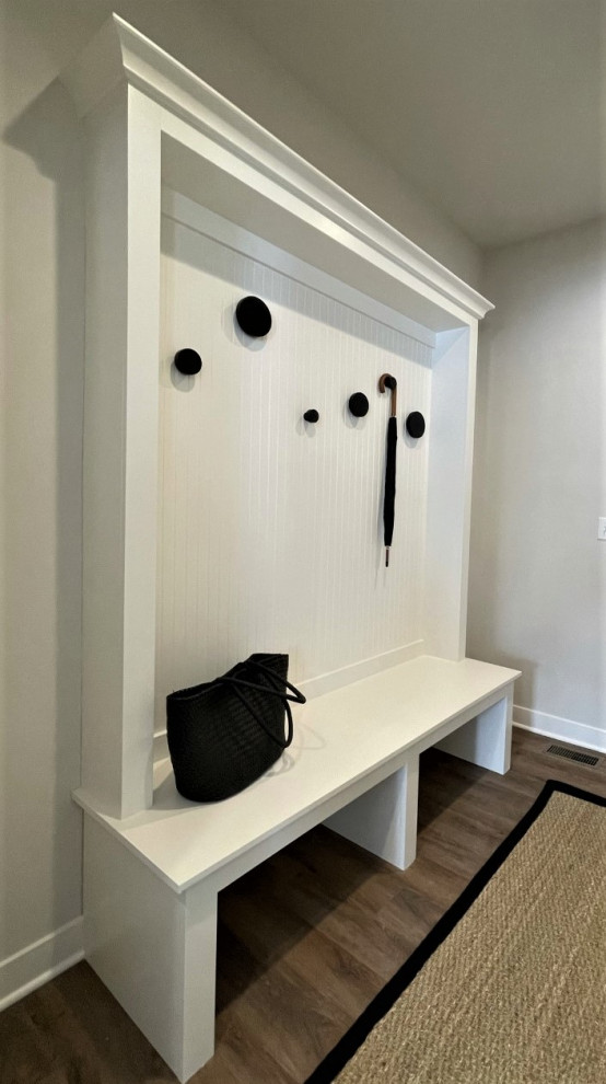 Aménagement d'une petite entrée classique avec un vestiaire, un mur blanc, un sol en vinyl, une porte simple et un sol marron.