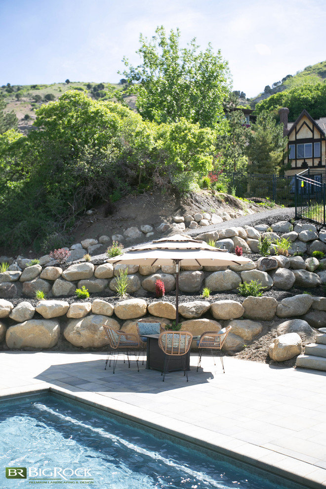 This is an example of an expansive contemporary backyard driveway in Salt Lake City with a retaining wall, natural stone pavers and a metal fence.