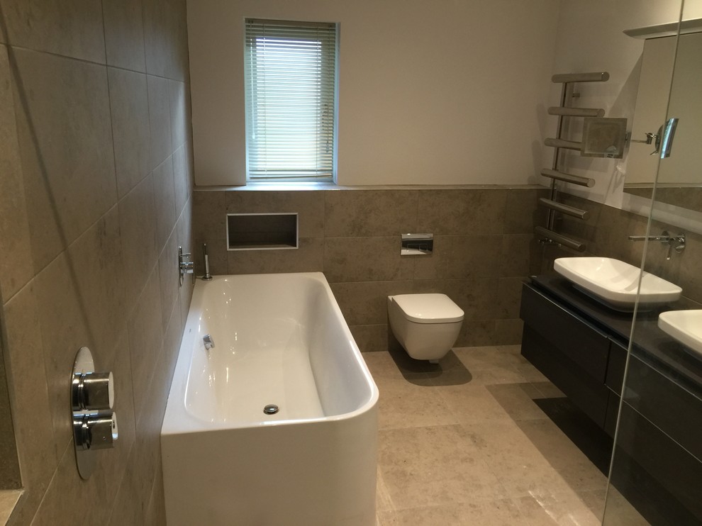 This is an example of a large contemporary master bathroom in Hampshire with dark wood cabinets, a drop-in tub, an open shower, a wall-mount toilet, gray tile, porcelain tile, white walls, porcelain floors, a console sink and quartzite benchtops.