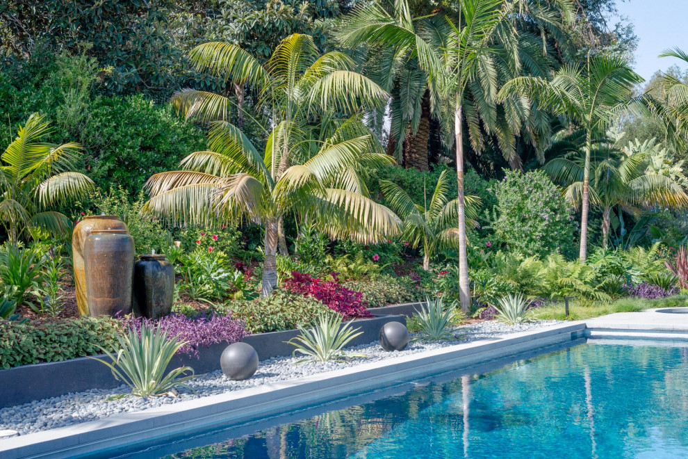 Cette photo montre un piscine avec aménagement paysager arrière exotique rectangle avec une terrasse en bois.
