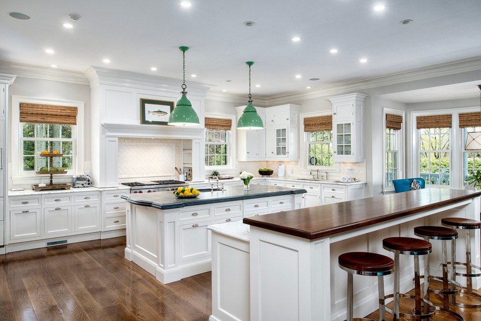 Photo of a traditional l-shaped kitchen in New York with an undermount sink, shaker cabinets, white cabinets, white splashback, ceramic splashback, stainless steel appliances, medium hardwood floors, multiple islands and wood benchtops.