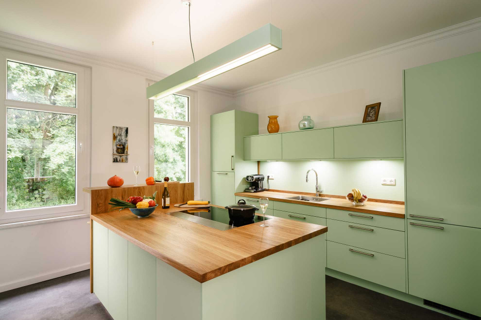 Inspiration for a mid-sized contemporary open plan kitchen in Bremen with an undermount sink, flat-panel cabinets, green cabinets, wood benchtops, green splashback, black appliances, laminate floors, with island, grey floor and brown benchtop.