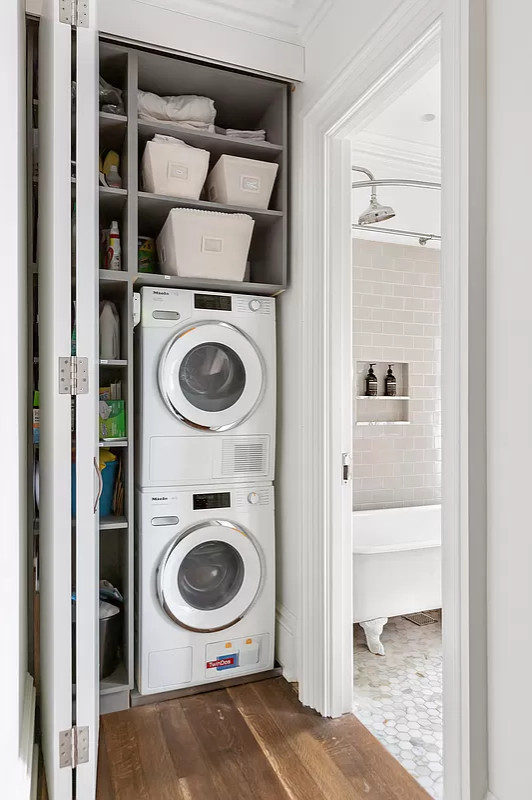 Einzeiliger, Kleiner Retro Hauswirtschaftsraum mit Waschmaschinenschrank, weißen Schränken und Waschmaschine und Trockner gestapelt in New York