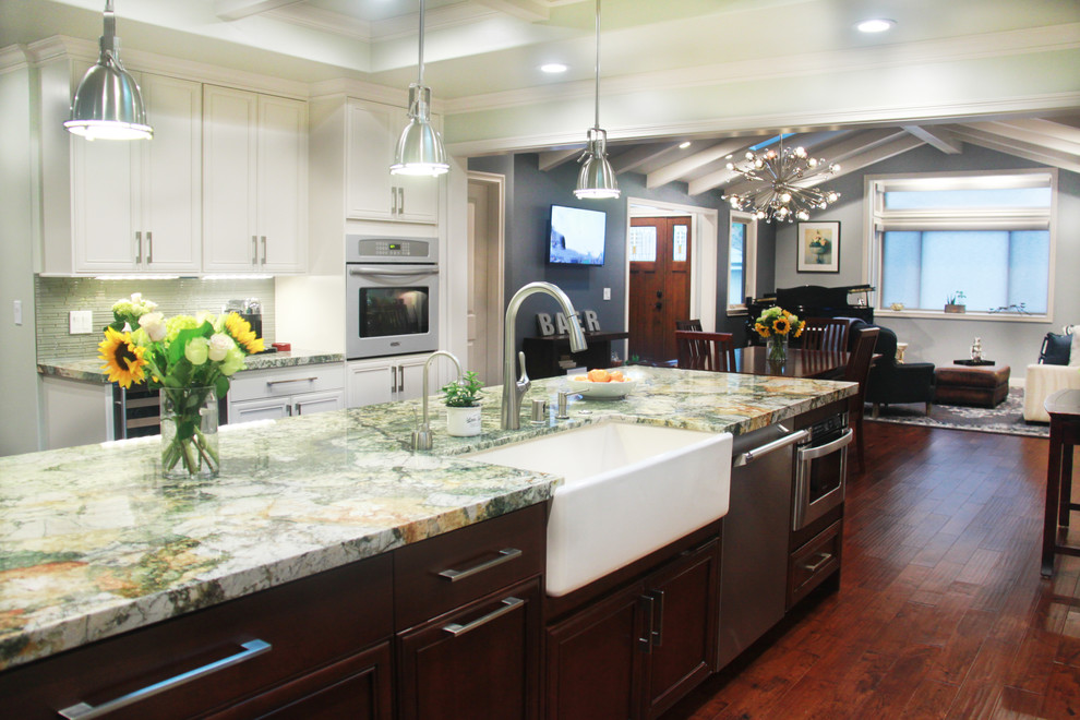Example of a mid-sized transitional u-shaped dark wood floor and brown floor eat-in kitchen design in San Francisco with a farmhouse sink, recessed-panel cabinets, white cabinets, granite countertops, green backsplash, glass tile backsplash, stainless steel appliances, an island and multicolored countertops
