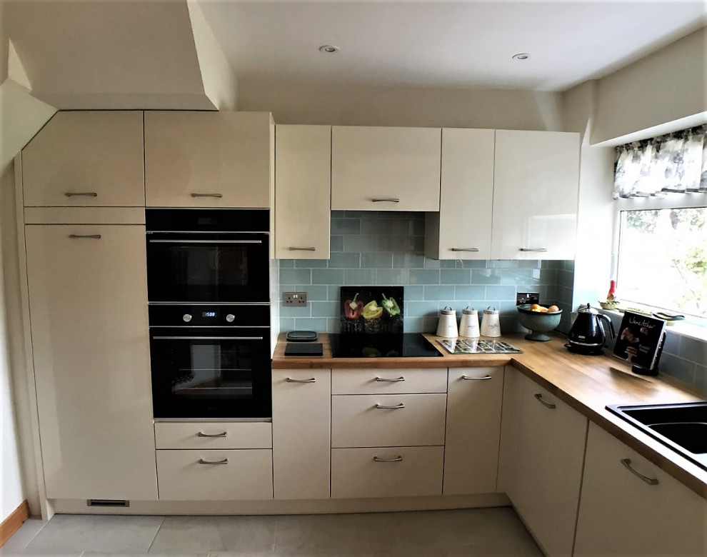 Photo of a small modern l-shaped eat-in kitchen in Other with flat-panel cabinets, wood benchtops, blue splashback, porcelain splashback, black appliances, porcelain floors, no island and grey floor.