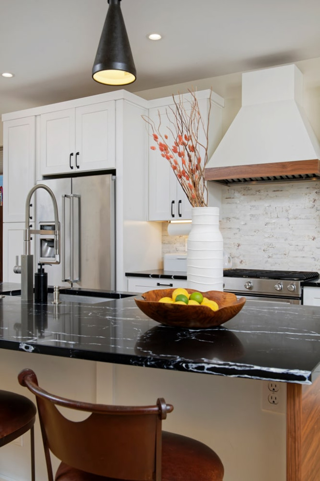 Photo of a mid-sized transitional l-shaped eat-in kitchen in Santa Barbara with an undermount sink, shaker cabinets, white splashback, stainless steel appliances, medium hardwood floors, with island and black benchtop.