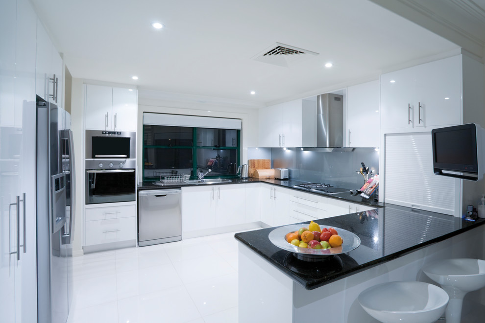 This is an example of a large contemporary u-shaped separate kitchen in Other with a drop-in sink, flat-panel cabinets, white cabinets, solid surface benchtops, grey splashback, a peninsula and stainless steel appliances.