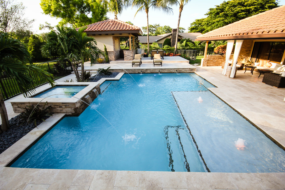 This is an example of a mid-sized contemporary backyard rectangular natural pool in Miami with a hot tub and natural stone pavers.