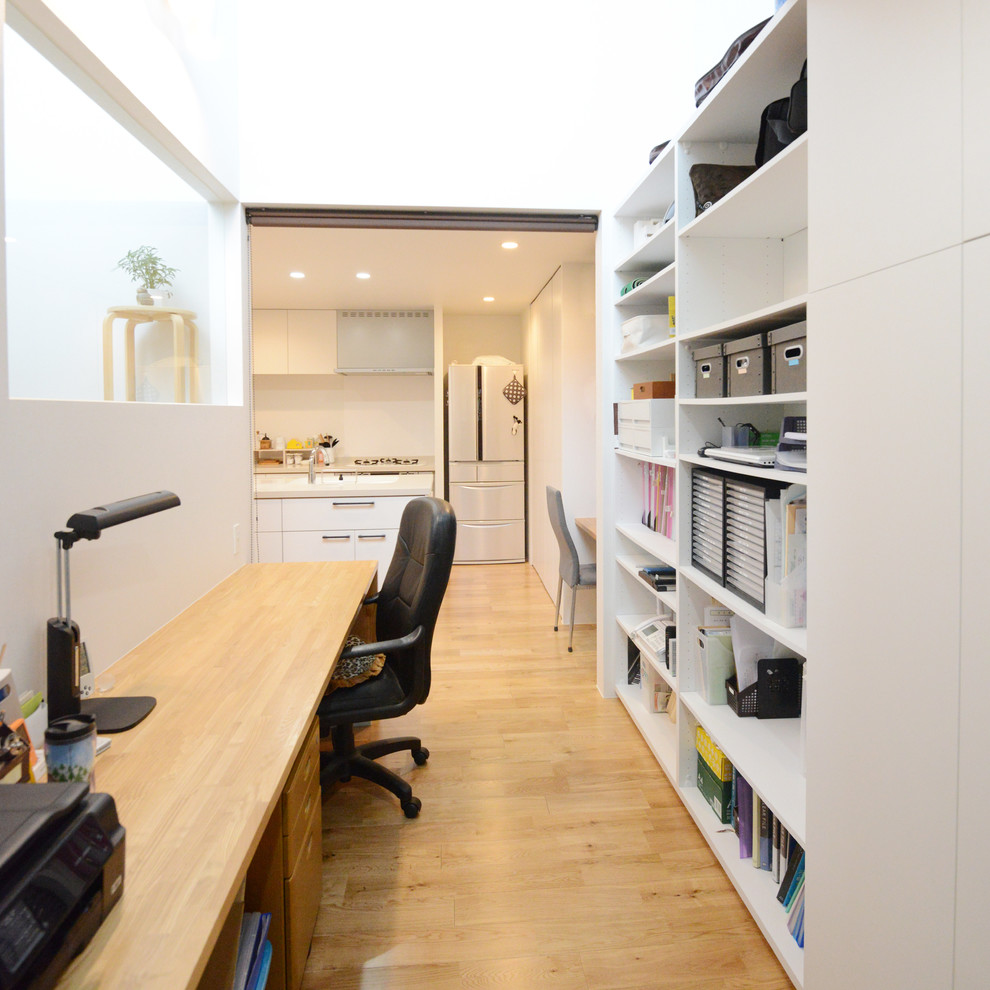 Contemporary home office in Yokohama with white walls, medium hardwood floors, a built-in desk and brown floor.