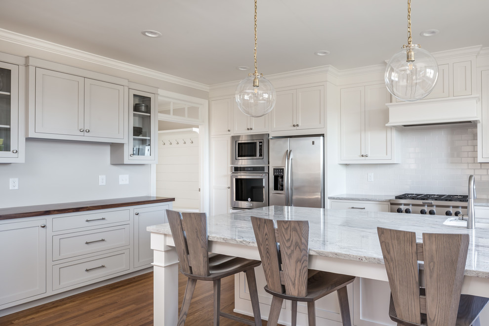 This is an example of a large transitional u-shaped eat-in kitchen in Raleigh with a farmhouse sink, shaker cabinets, white cabinets, white splashback, stainless steel appliances, medium hardwood floors, with island, brown floor, quartzite benchtops, subway tile splashback and white benchtop.