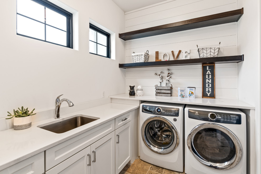 Design ideas for a country l-shaped dedicated laundry room in Cincinnati with an undermount sink, white cabinets, quartz benchtops, white walls, travertine floors, a side-by-side washer and dryer, white benchtop, recessed-panel cabinets and beige floor.