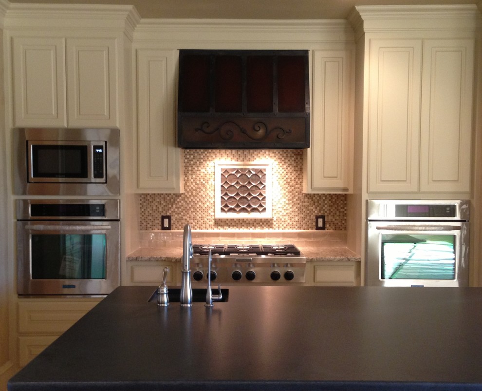 Inspiration for a mid-sized rustic galley travertine floor eat-in kitchen remodel in Austin with an undermount sink, raised-panel cabinets, medium tone wood cabinets, granite countertops, beige backsplash, stone tile backsplash, stainless steel appliances and an island