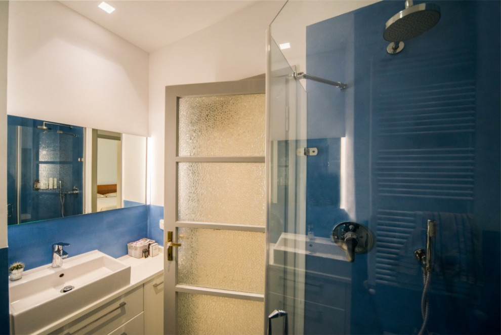 Foto på ett mellanstort funkis vit badrum, med släta luckor, blå skåp, en vägghängd toalettstol, blå kakel, blå väggar, betonggolv, ett fristående handfat, träbänkskiva och grått golv