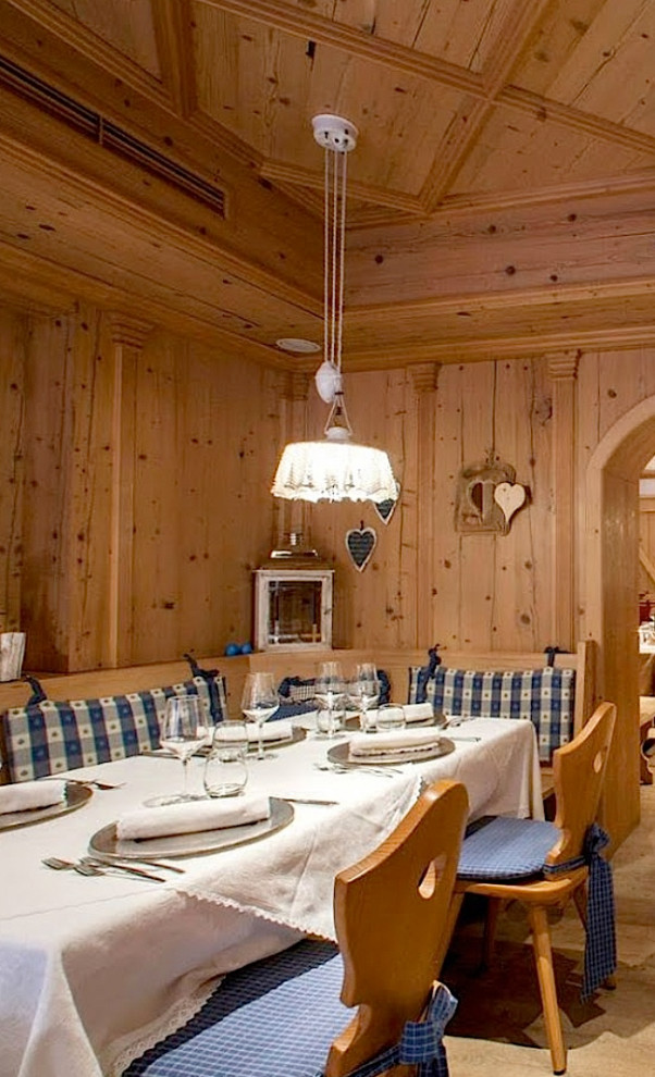 Immagine di una grande sala da pranzo aperta verso la cucina stile rurale con pareti marroni, pavimento in legno verniciato, stufa a legna, pavimento beige, soffitto in legno e pareti in legno