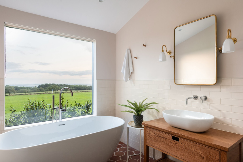 Mid-sized country bathroom in Other with brown cabinets, a freestanding tub, white tile, white walls, terra-cotta floors, wood benchtops, red floor, brown benchtops, subway tile, a vessel sink and flat-panel cabinets.