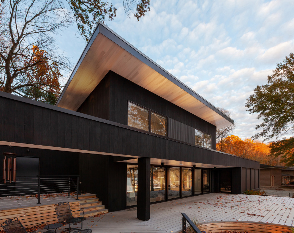 Esempio della facciata di una casa nera moderna a due piani di medie dimensioni con rivestimento in legno, copertura in metallo o lamiera, tetto grigio, pannelli sovrapposti e terreno in pendenza