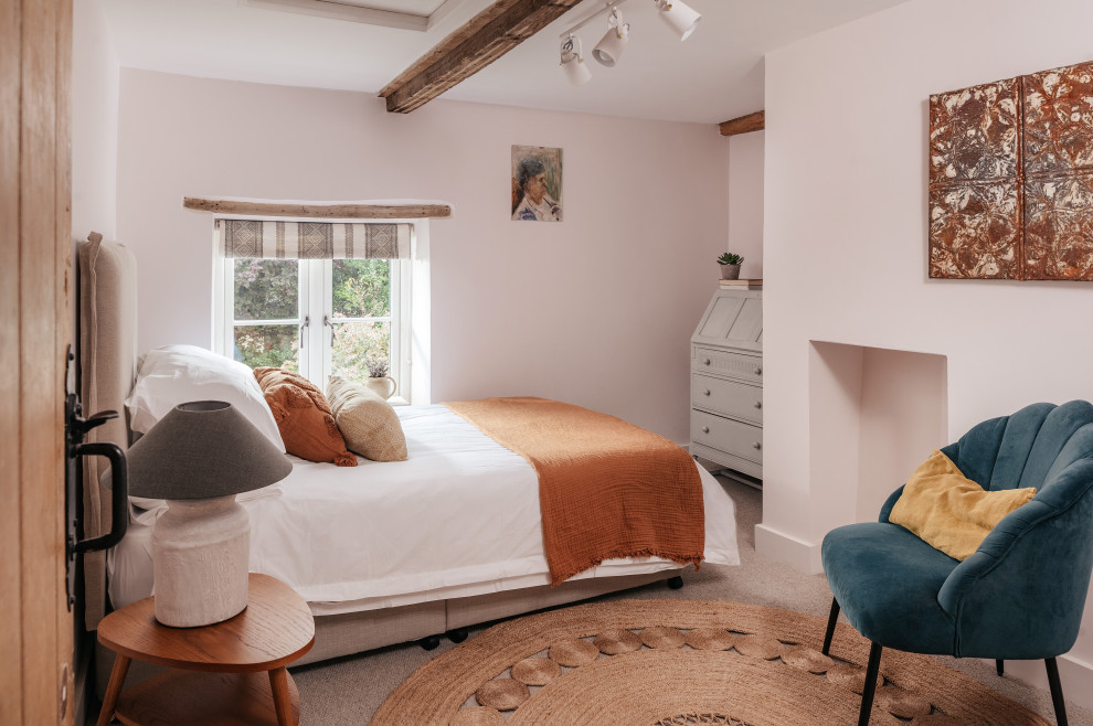 Large country guest bedroom in Gloucestershire with white walls, carpet, beige floors and exposed beams.
