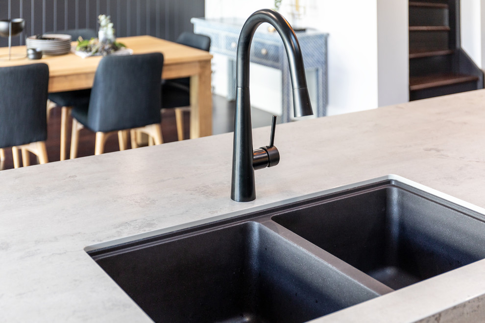 This is an example of a mid-sized galley kitchen pantry in Adelaide with a double-bowl sink, black cabinets, concrete benchtops, white splashback, stone slab splashback, black appliances, dark hardwood floors, with island, brown floor and grey benchtop.