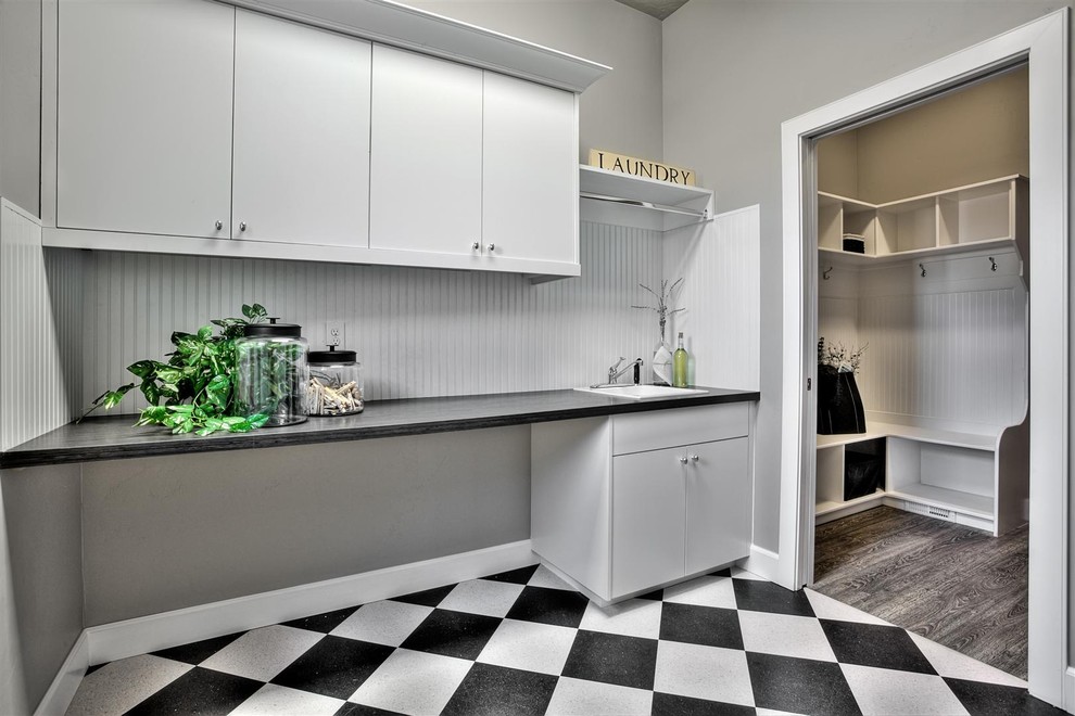 This is an example of a large transitional single-wall dedicated laundry room in Boise with a drop-in sink, flat-panel cabinets, white cabinets, wood benchtops, grey walls, vinyl floors, a side-by-side washer and dryer and black benchtop.