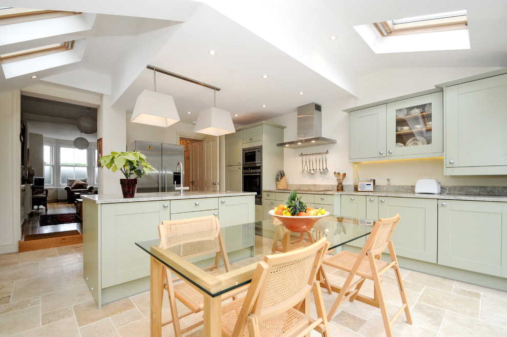 This is an example of a mid-sized transitional l-shaped eat-in kitchen in London with an undermount sink, shaker cabinets, green cabinets, granite benchtops, stone slab splashback, stainless steel appliances, travertine floors, with island and beige floor.