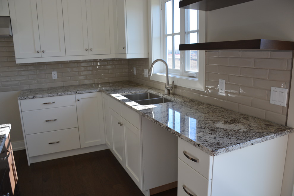 Inspiration for a mid-sized transitional u-shaped light wood floor eat-in kitchen remodel in Toronto with a double-bowl sink, shaker cabinets, white cabinets, granite countertops, gray backsplash, subway tile backsplash, stainless steel appliances and an island