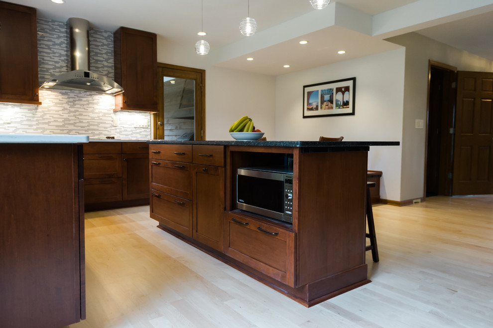 Large transitional l-shaped light wood floor eat-in kitchen photo with an undermount sink, shaker cabinets, dark wood cabinets, quartz countertops, gray backsplash, matchstick tile backsplash, stainless steel appliances and an island