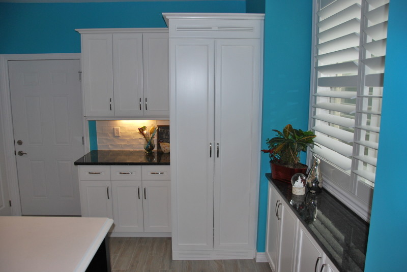 Inspiration for a mid-sized transitional l-shaped porcelain tile and beige floor kitchen remodel in Toronto with an undermount sink, recessed-panel cabinets, white cabinets, granite countertops, white backsplash, subway tile backsplash, stainless steel appliances, an island and black countertops