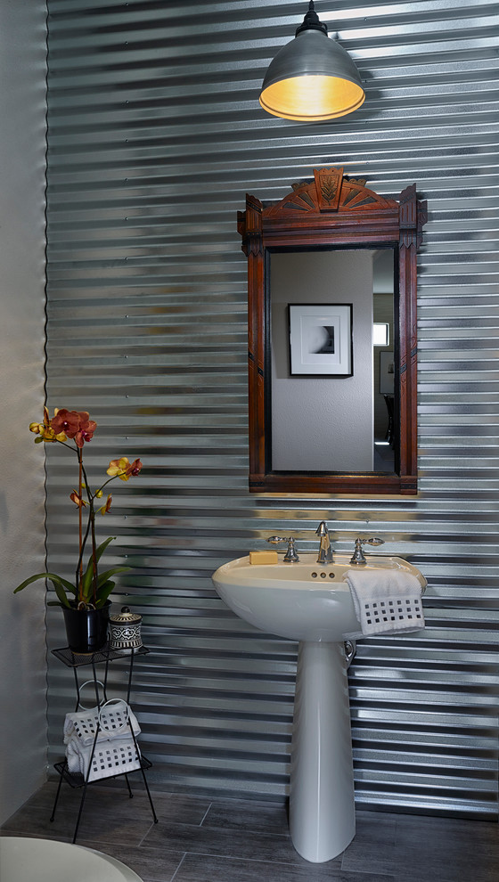 This is an example of a small industrial powder room in Los Angeles with a pedestal sink, grey walls and porcelain floors.