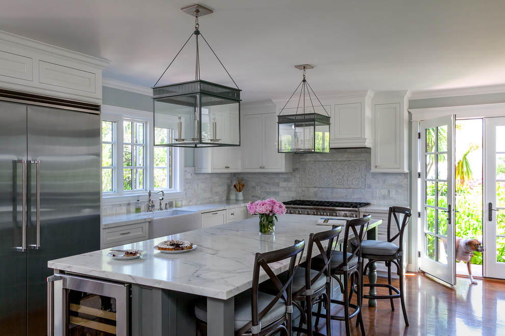 This is an example of a transitional l-shaped kitchen in San Francisco with a farmhouse sink, recessed-panel cabinets, white cabinets, grey splashback, stainless steel appliances, dark hardwood floors and with island.