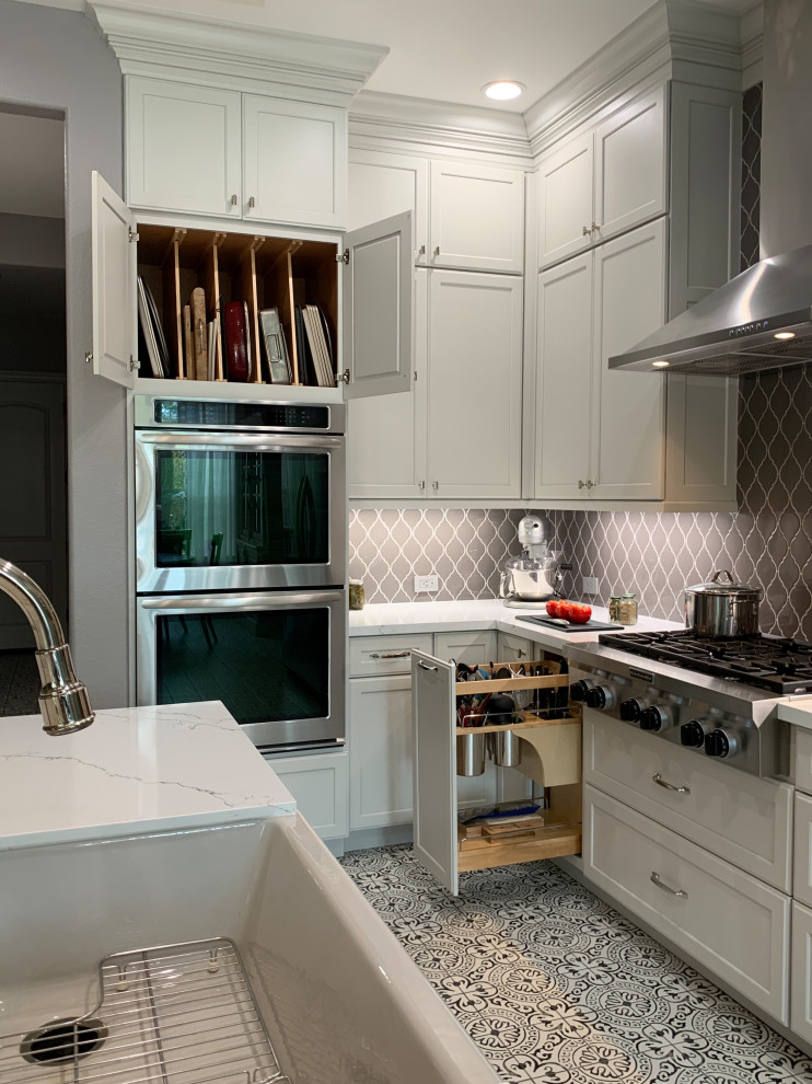 Transitional l-shaped porcelain tile and multicolored floor kitchen photo in Houston with a farmhouse sink, recessed-panel cabinets, white cabinets, quartz countertops, gray backsplash, ceramic backsplash, stainless steel appliances, an island and white countertops
