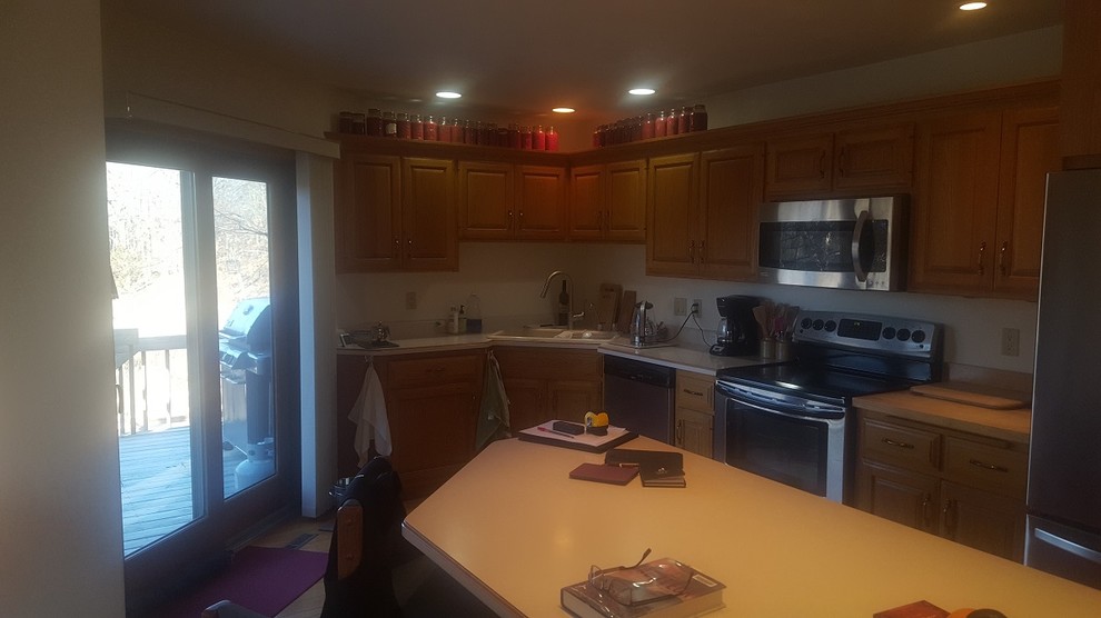 Example of a transitional light wood floor and beige floor kitchen pantry design with a double-bowl sink, raised-panel cabinets, light wood cabinets, laminate countertops, stainless steel appliances, an island and white countertops