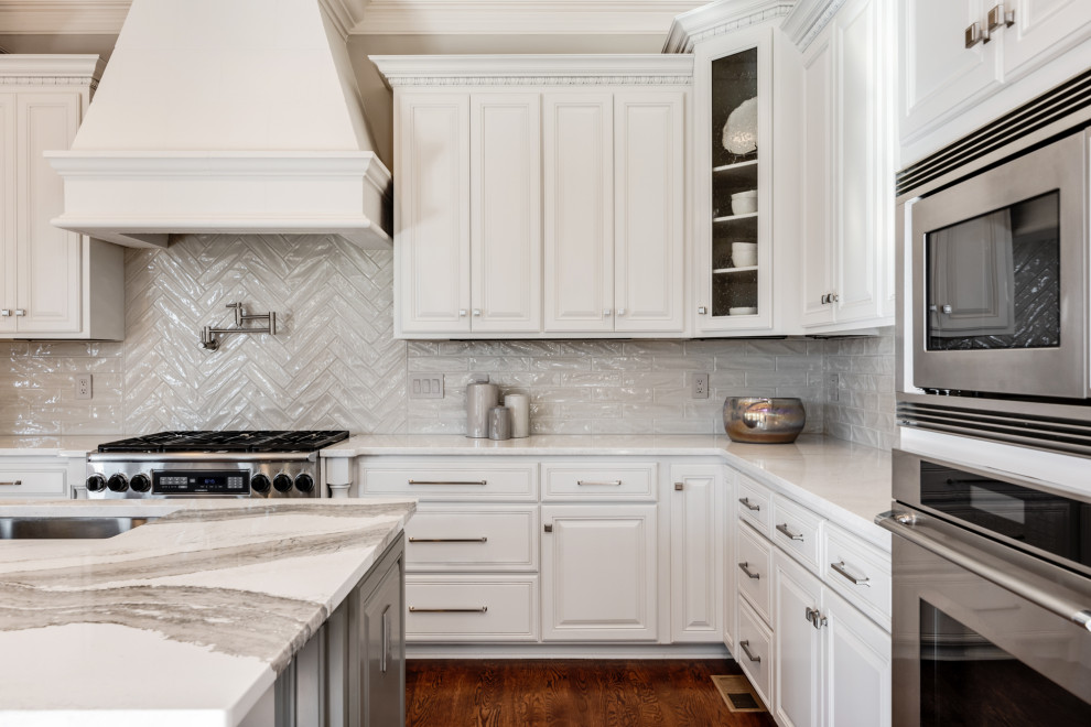 Design ideas for a large transitional l-shaped eat-in kitchen in Charlotte with an undermount sink, raised-panel cabinets, white cabinets, quartz benchtops, grey splashback, porcelain splashback, stainless steel appliances, dark hardwood floors, with island, brown floor and white benchtop.