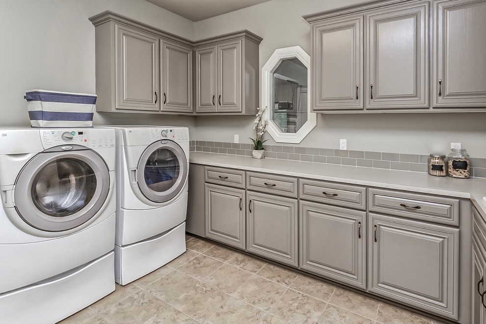 Mid-sized beach style l-shaped dedicated laundry room in Omaha with a drop-in sink, raised-panel cabinets, grey cabinets, laminate benchtops, grey walls, porcelain floors and a side-by-side washer and dryer.