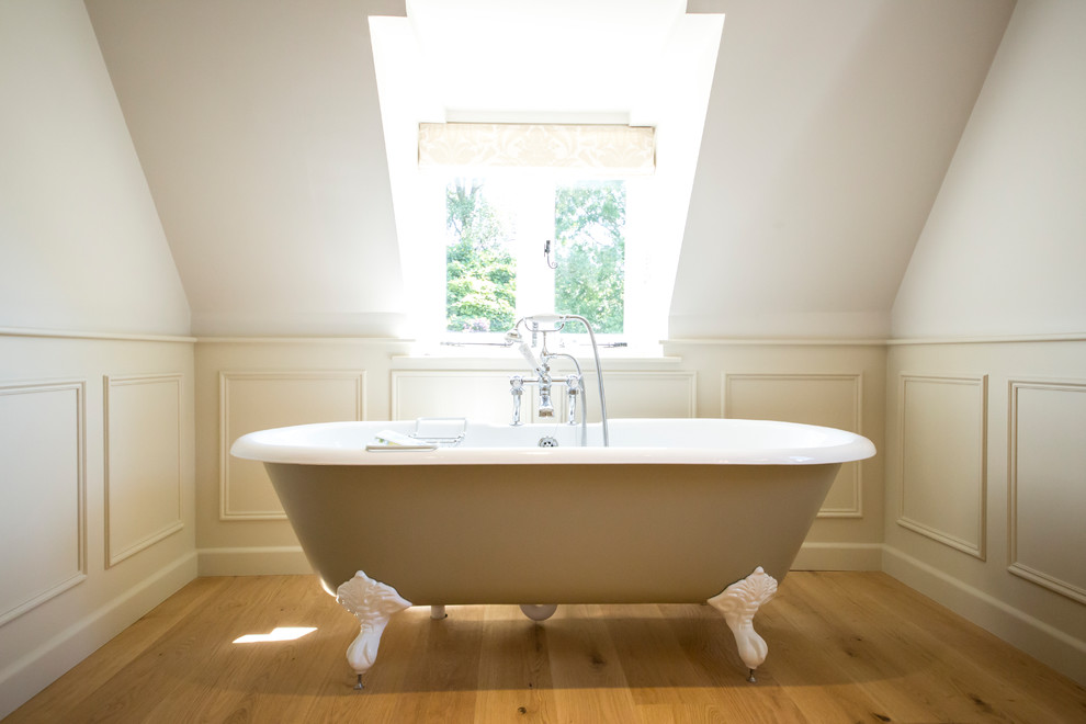 Inspiration pour une salle de bain beige et blanche rustique pour enfant avec une baignoire sur pieds, un carrelage beige, un mur blanc, un sol en bois brun, un sol marron, une fenêtre et un plafond voûté.