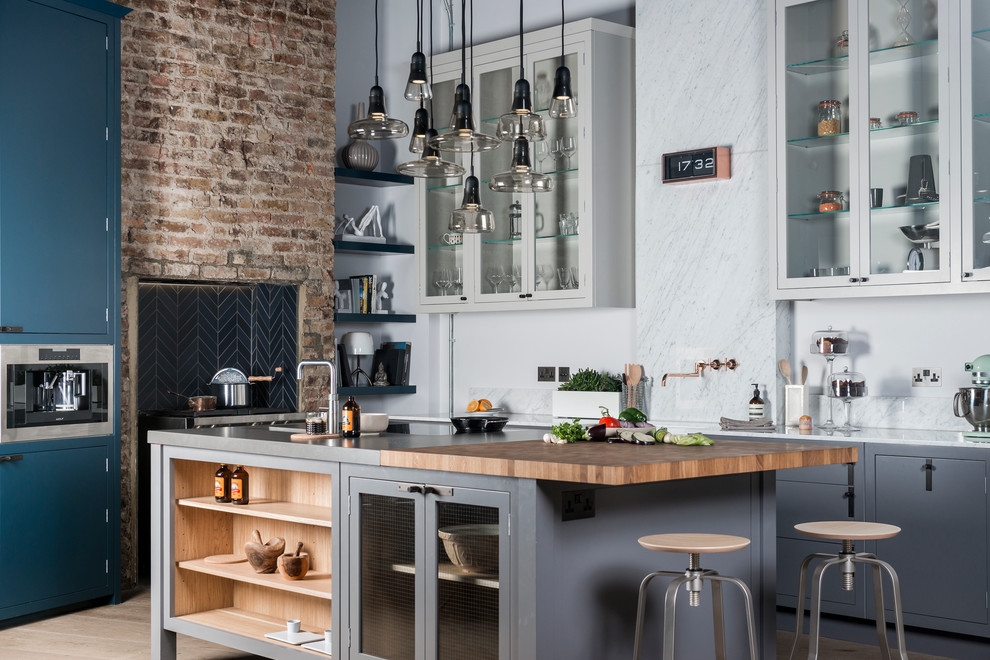 This is an example of a mid-sized industrial eat-in kitchen in London with grey cabinets, marble benchtops, grey splashback, stone slab splashback, with island and stainless steel appliances.