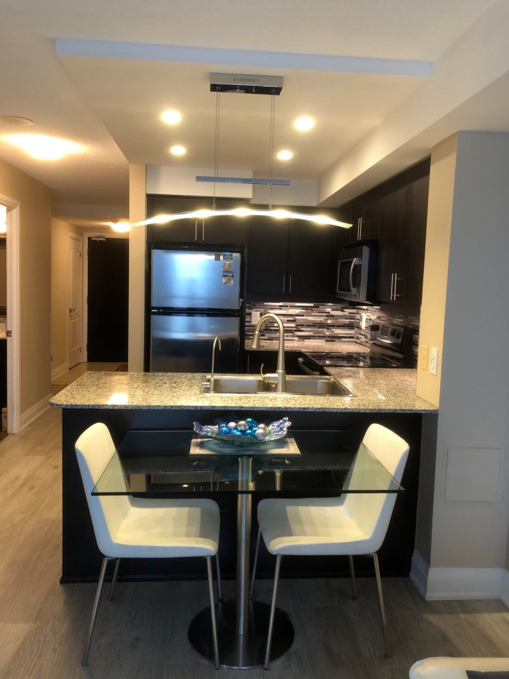 This is an example of a small transitional u-shaped open plan kitchen in Toronto with a drop-in sink, flat-panel cabinets, dark wood cabinets, granite benchtops, multi-coloured splashback, mosaic tile splashback, stainless steel appliances, porcelain floors, a peninsula, beige floor and multi-coloured benchtop.
