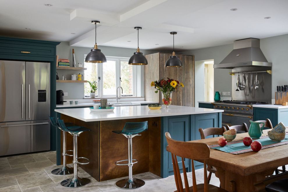 Country l-shaped kitchen in London with a belfast sink, beaded cabinets, blue cabinets, stainless steel appliances, an island, grey floors and white worktops.