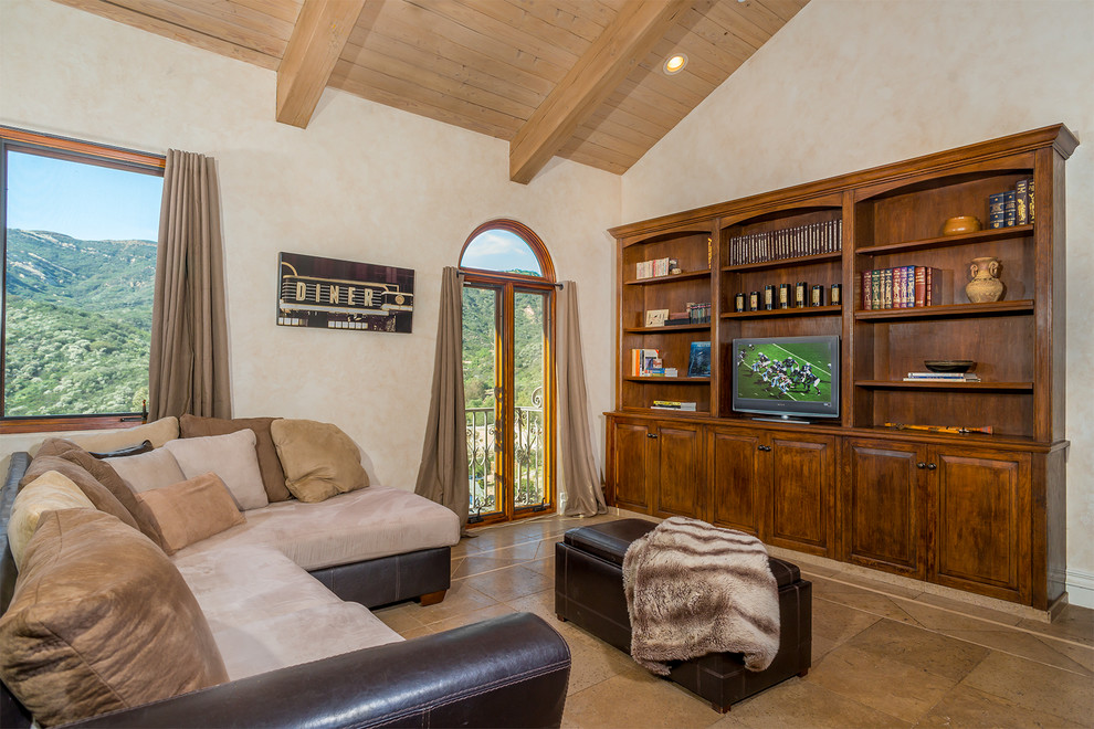 This is an example of a mid-sized mediterranean open concept family room in Los Angeles with beige walls, terra-cotta floors, a built-in media wall, a home bar, no fireplace and beige floor.