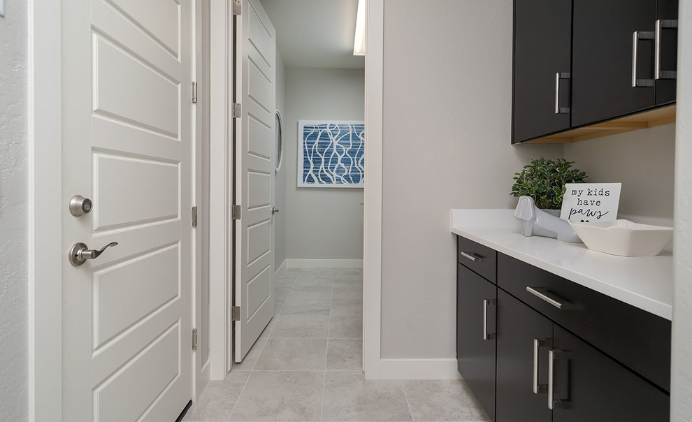 Photo of a large contemporary single-wall dedicated laundry room in Phoenix with flat-panel cabinets, dark wood cabinets, solid surface benchtops, beige walls, ceramic floors, a side-by-side washer and dryer, beige floor and white benchtop.