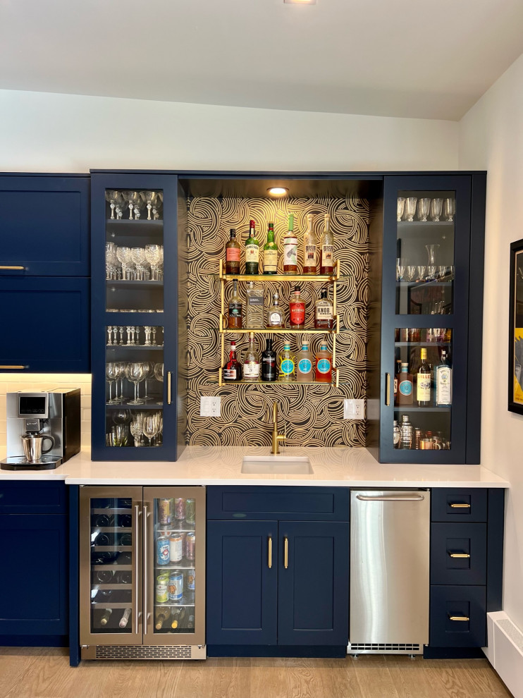 Inspiration for a small modern single-wall wet bar in Denver with a submerged sink, glass-front cabinets, blue cabinets, engineered stone countertops, black splashback, light hardwood flooring, grey floors and white worktops.