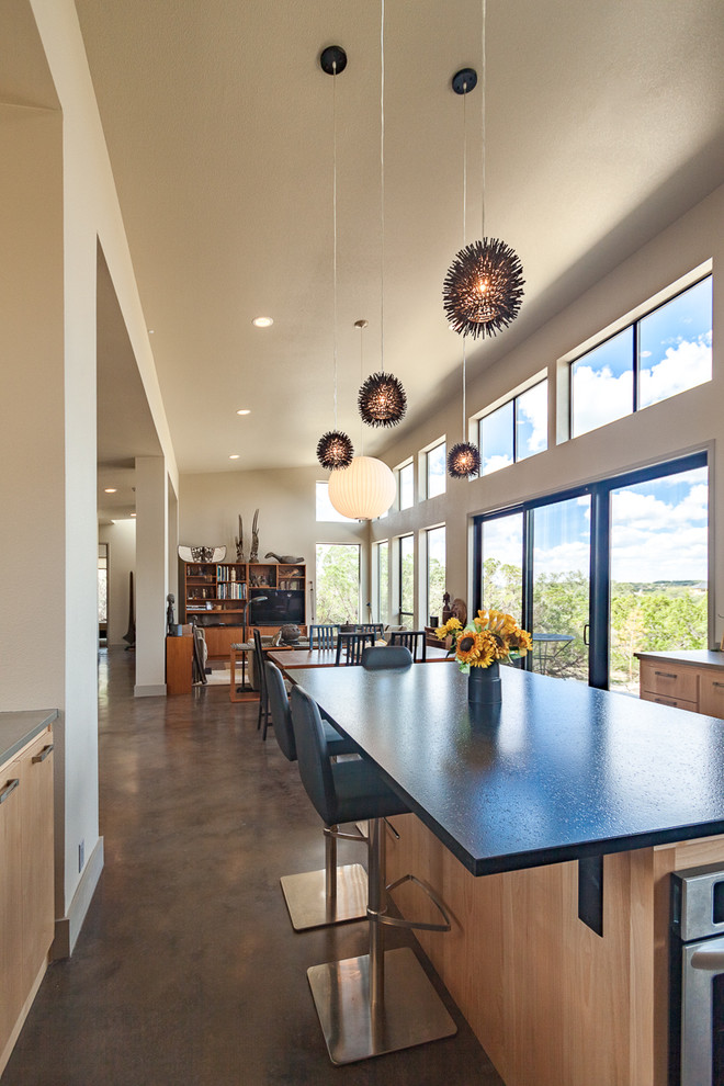 This is an example of a mid-sized contemporary l-shaped open plan kitchen in Austin with a double-bowl sink, flat-panel cabinets, light wood cabinets, granite benchtops, grey splashback, stainless steel appliances, concrete floors and with island.