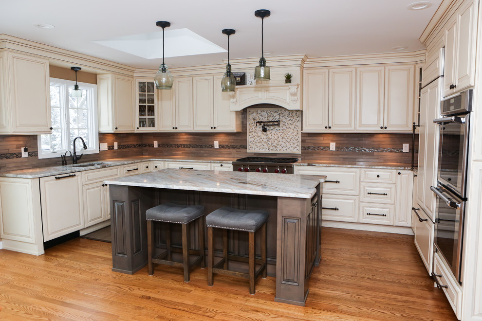 Large transitional u-shaped light wood floor eat-in kitchen photo in Newark with an undermount sink, raised-panel cabinets, distressed cabinets, granite countertops, brown backsplash, mosaic tile backsplash, stainless steel appliances and an island