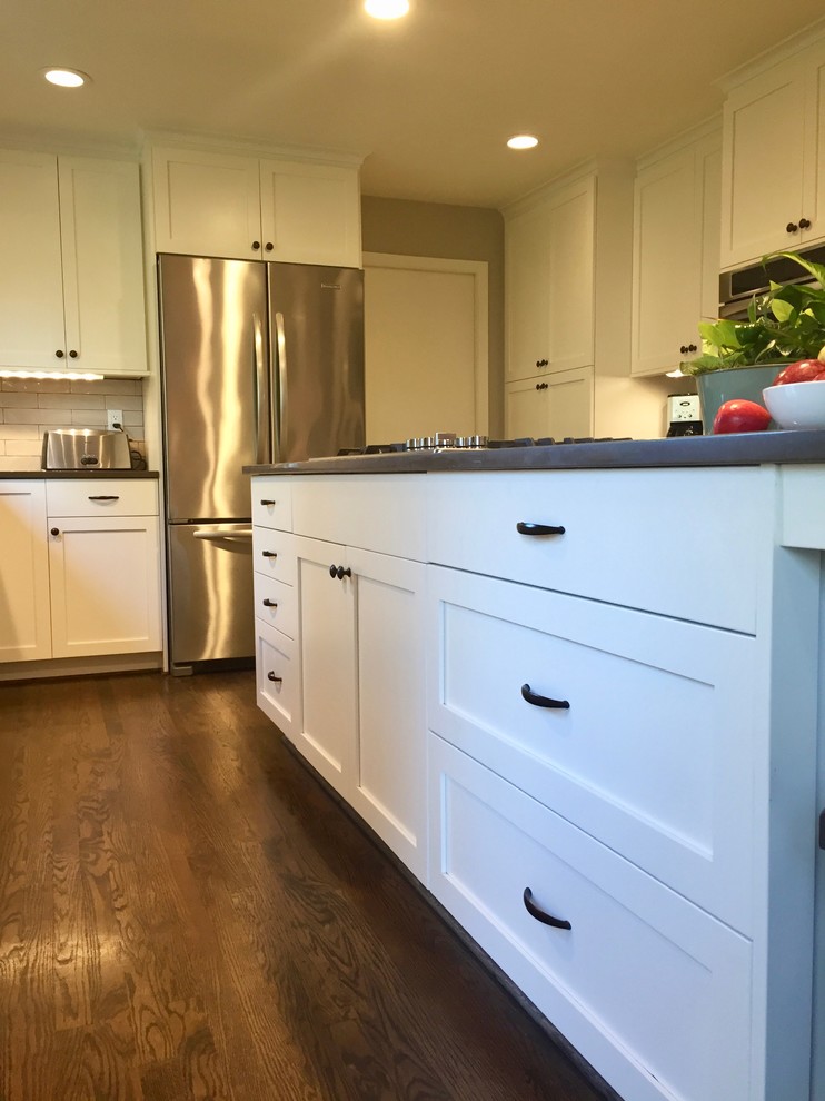 Photo of a mid-sized traditional l-shaped open plan kitchen in Portland with an undermount sink, shaker cabinets, white cabinets, quartz benchtops, beige splashback, subway tile splashback, stainless steel appliances, medium hardwood floors, with island and brown benchtop.