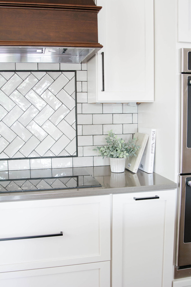 Eat-in kitchen - mid-sized transitional l-shaped medium tone wood floor and brown floor eat-in kitchen idea in Omaha with a farmhouse sink, shaker cabinets, white cabinets, quartzite countertops, white backsplash, subway tile backsplash, stainless steel appliances, an island and white countertops
