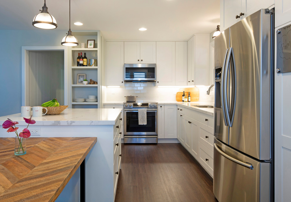 This is an example of a mid-sized transitional l-shaped eat-in kitchen in Hawaii with an undermount sink, shaker cabinets, white cabinets, quartz benchtops, grey splashback, ceramic splashback, stainless steel appliances, vinyl floors, with island, brown floor and white benchtop.