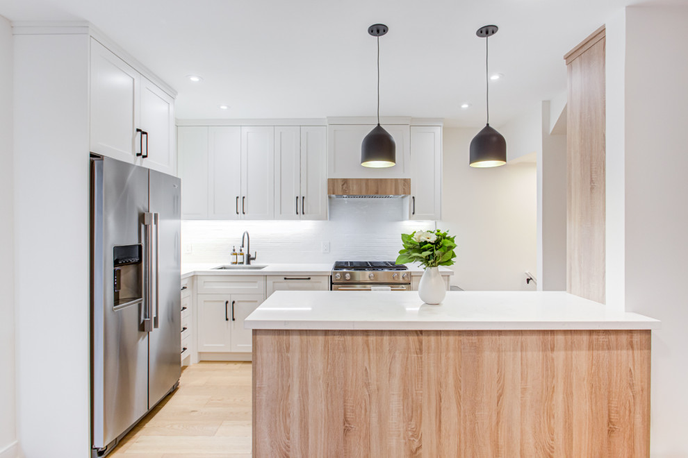 This is an example of a scandinavian kitchen in Toronto with a single-bowl sink, shaker cabinets, white cabinets, engineered stone countertops, white splashback, metro tiled splashback, light hardwood flooring and white worktops.