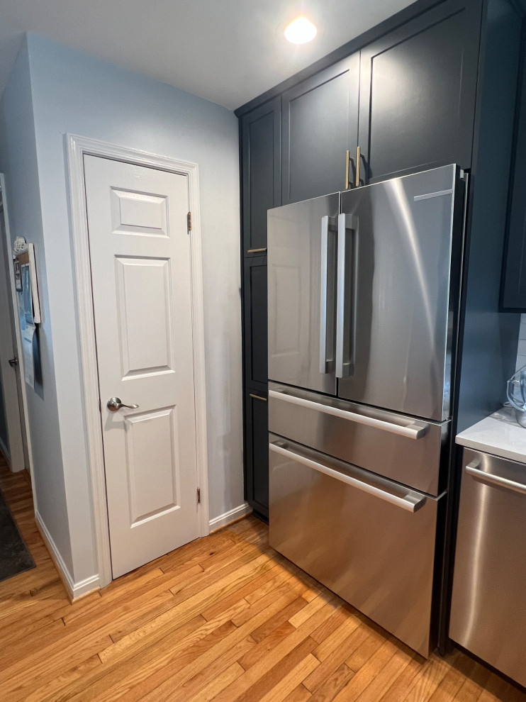 Photo of a small traditional u-shaped open plan kitchen in Baltimore with a submerged sink, shaker cabinets, blue cabinets, engineered stone countertops, white splashback, porcelain splashback, stainless steel appliances, medium hardwood flooring, a breakfast bar, brown floors and white worktops.