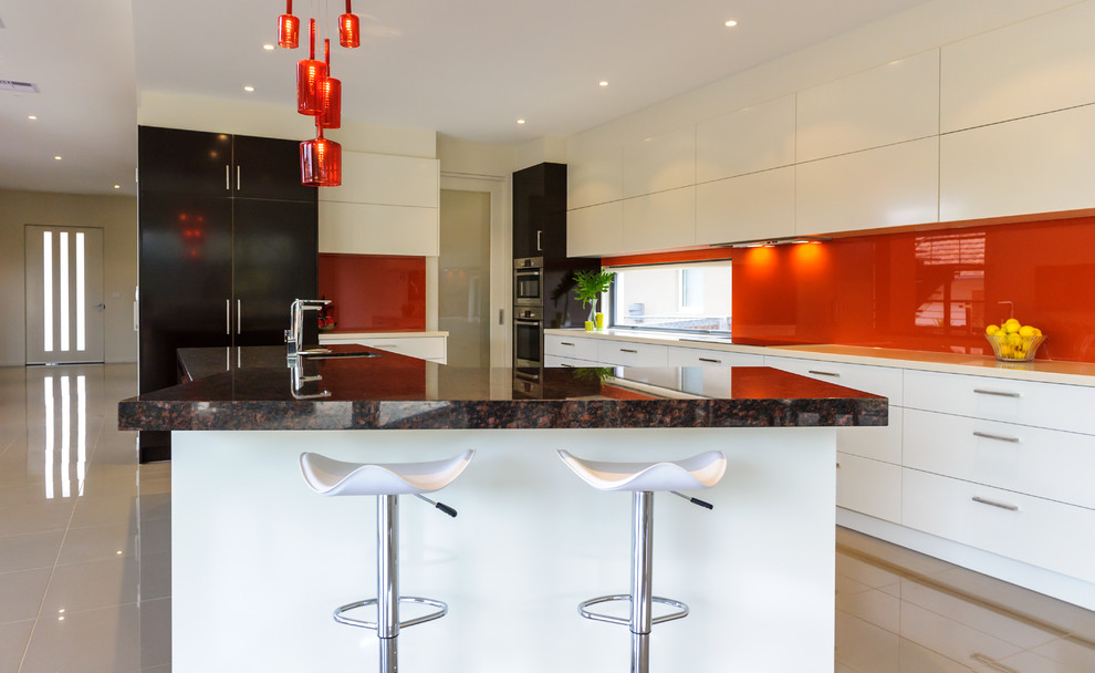 This is an example of a large contemporary open plan kitchen in Melbourne with an undermount sink, flat-panel cabinets, white cabinets, glass benchtops, red splashback, glass sheet splashback, porcelain floors and with island.